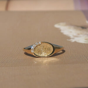 Deze ring van het merk Minioro bestaat uit 14 karaats goud en heeft een stuk waarin een vingerafdruk of gravering kan worden. Zo ontstaat een elegant en persoonlijk aandenken vol betekenis, afgewerkt met schitterende diamanten.