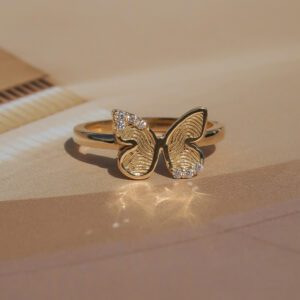 Deze ring van het merk Minioro bestaat uit 14 karaats goud en heeft een vlinderbedel waarin een vingerafdruk of gravering kan worden. Zo ontstaat een elegant en persoonlijk aandenken vol betekenis, afgewerkt met schitterende diamanten.